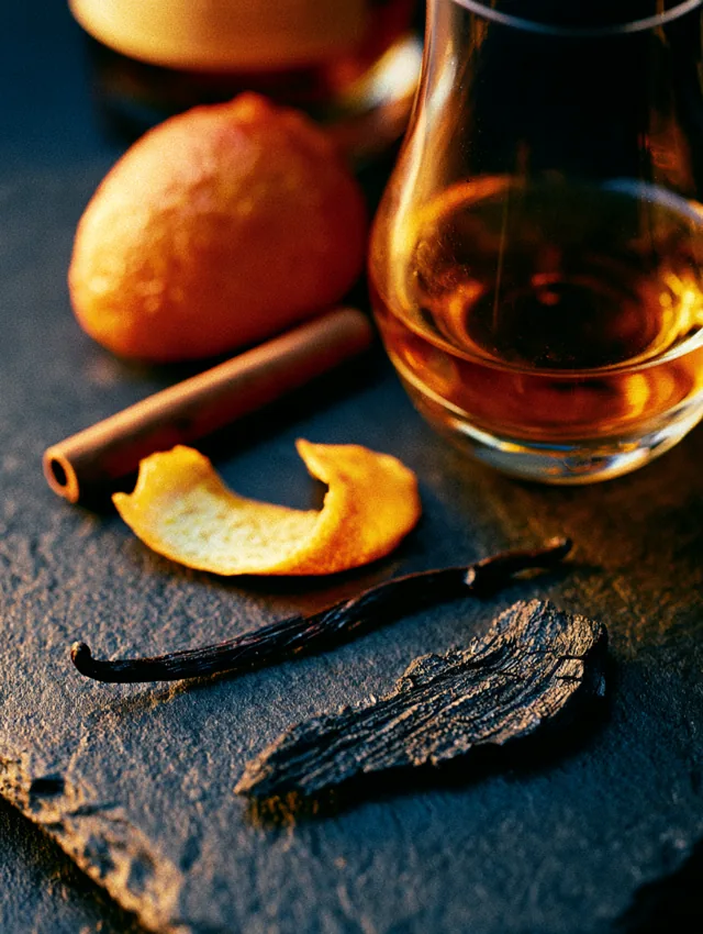 A glass of whiskey surrounded by flavor notes — apple, citrus peel, cinnamon, vanilla, and charred oak